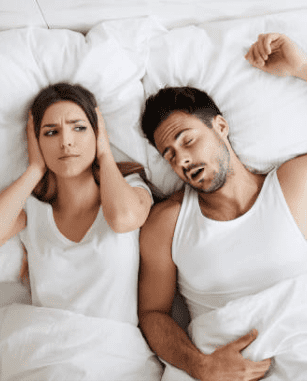 Couple in bed woman closing her ears due to husbands snoring