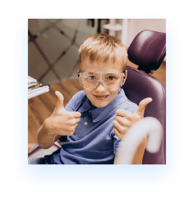 young boy sitting in dentist chair smiling with thumbs up