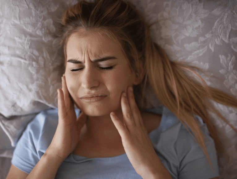 Woman in bed holding jaw because of bruxism pain
