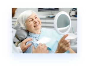 Older woman in the dental chair holding a mirror and looking at her teeth Restorative Dentistry