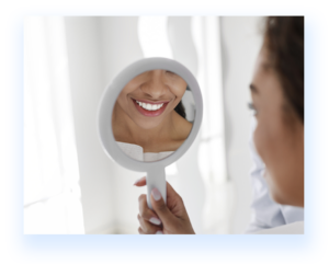 A woman holding and looking in the mirror checking her teeth